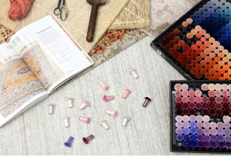 Interior designer working with a client or artisan — table spread with custom color tufts (yarn pom-poms), color pom swatches, custom rug rendering blueprints, and sample rug strike-offs.